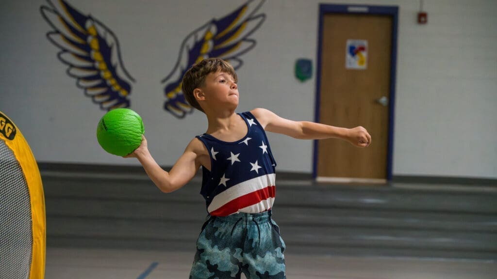 A young boy, in an indoor court, prepares to throw a ball during a game of handball at Kyle Summer Camp.
