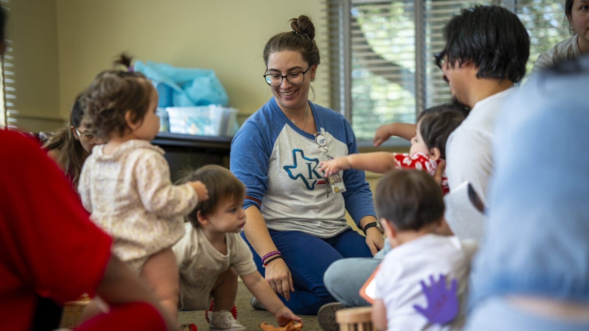 A woman sitting on the floor with many children for a library storytime.