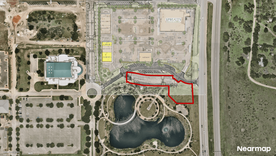Aerial view of a shopping center with a large parking lot, labeled "Sprouts," adjacent to a park with ponds and walking paths. A section near the park is outlined in red. Roads and greenery surround the area.