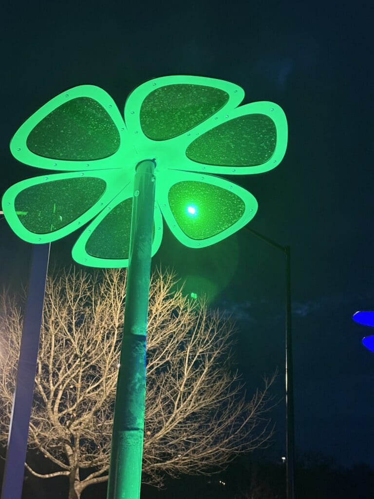 A large, green, clover-shaped light fixture glows at night as part of the Sky Blooms art installation at Steeplechase Park. 