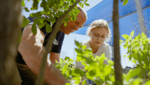 Conservation Division Manager John Davis and his daughter are pictured gardening together, surrounded by green plants under a blue canopy on a sunny day.