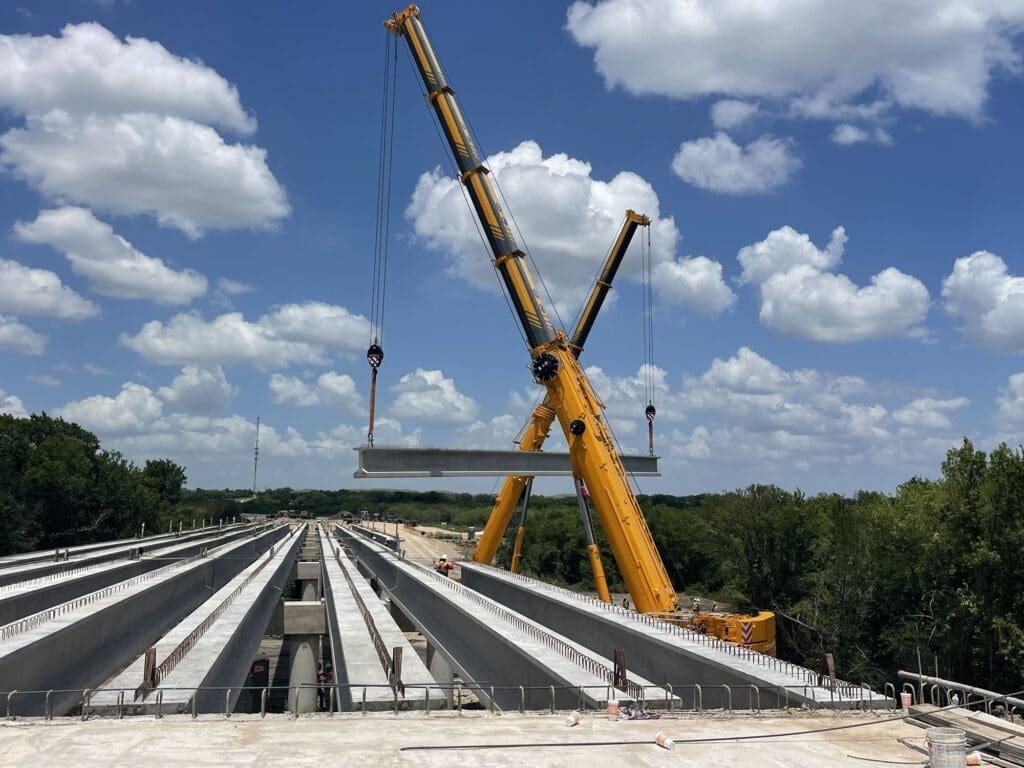 Two yellow cranes lift a large steel beam as part of building the new Kohlers to Seton extension in Kyle, Texas. 